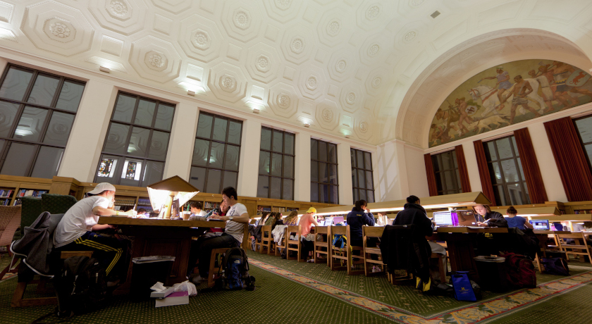 Many students are studying in a room by the dim light of their laptops