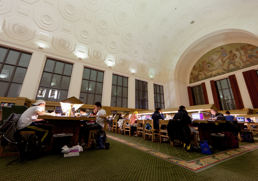 Many students are studying in a room by the dim light of their laptops