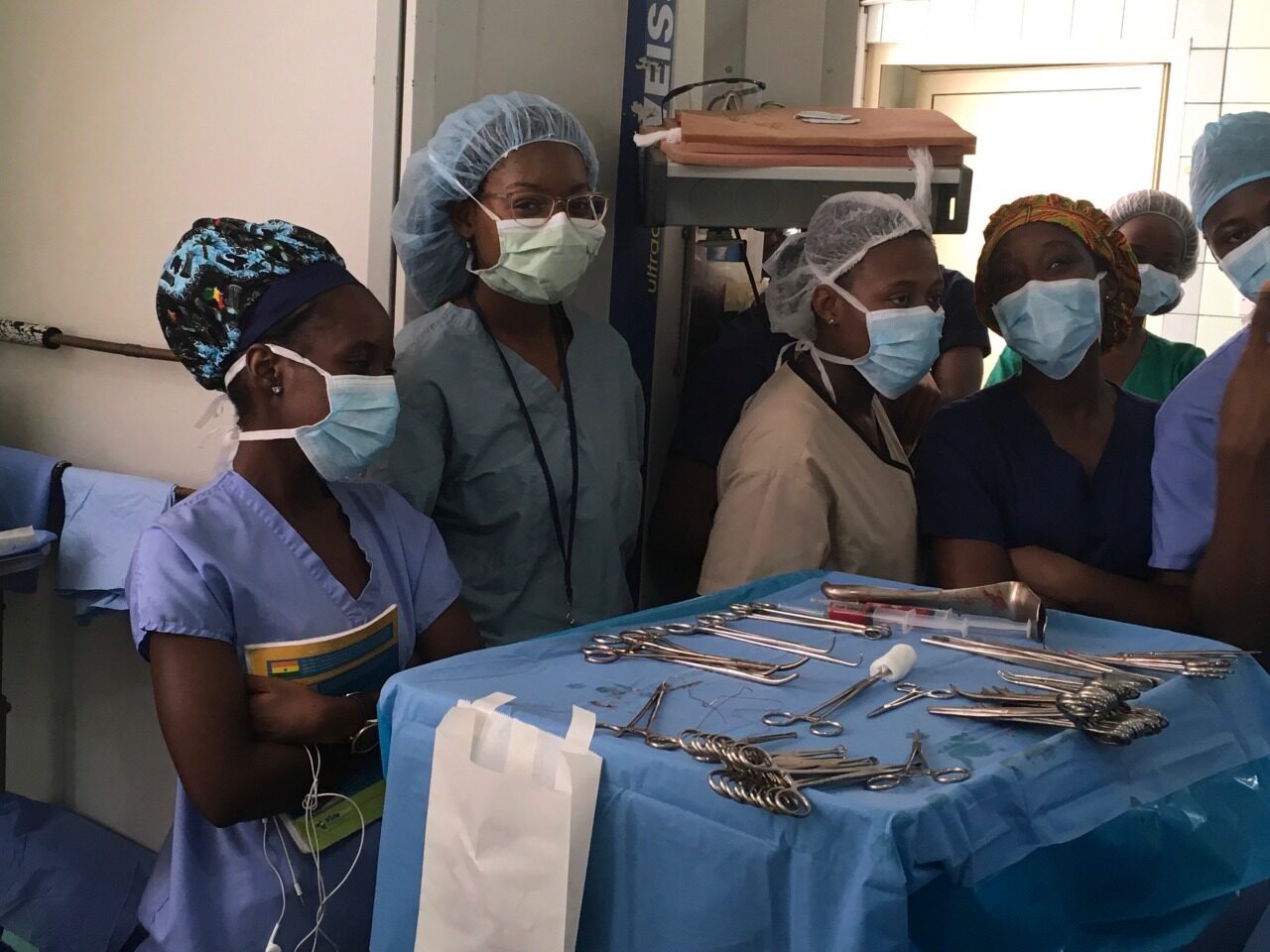 A group of medical personnel in hair caps and surgical masks behind a tray of surgical tools