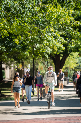 man with a face mask riding a bicycle through campus